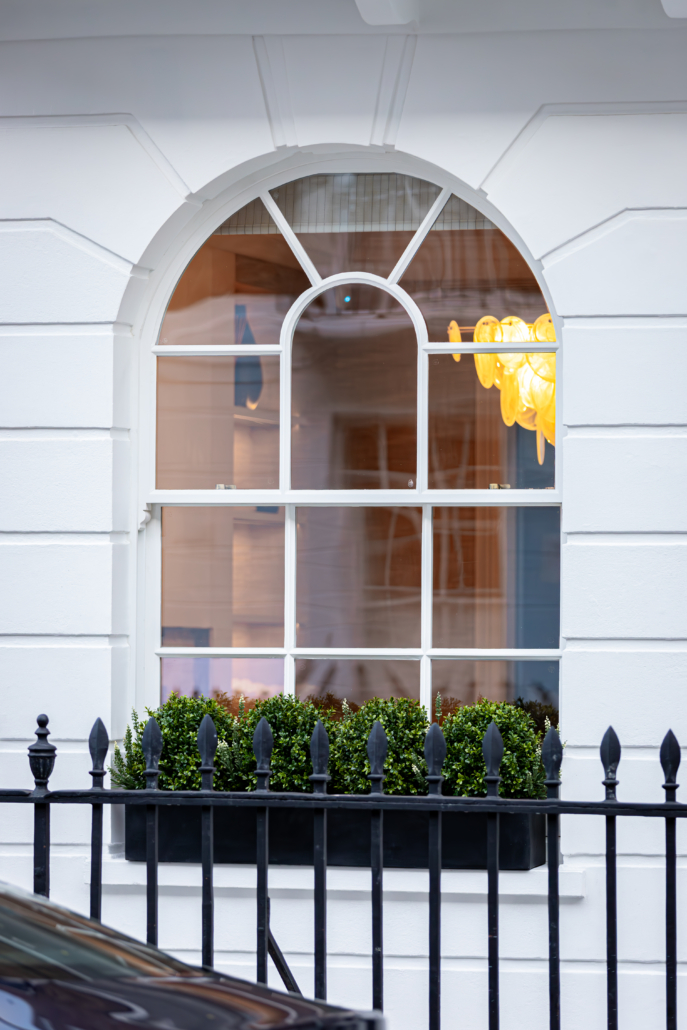 An arched timber sash window with slim glazing bars in a white rendered wall, behind black railings